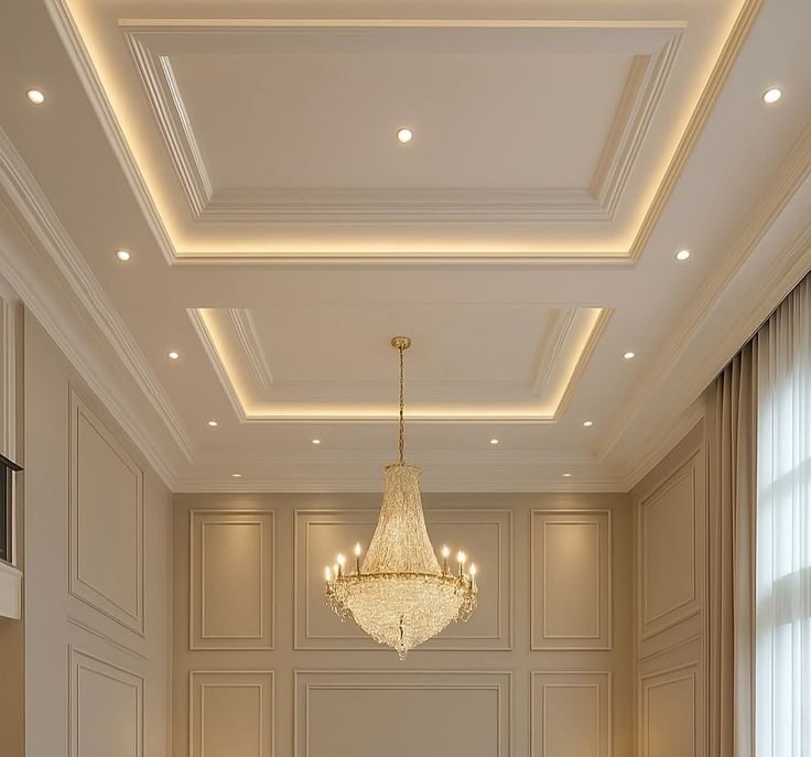Classic living room featuring an elegant drop ceiling with recessed LED lighting, detailed ceiling molding, and a crystal chandelier above a symmetrical seating arrangement in neutral tones.