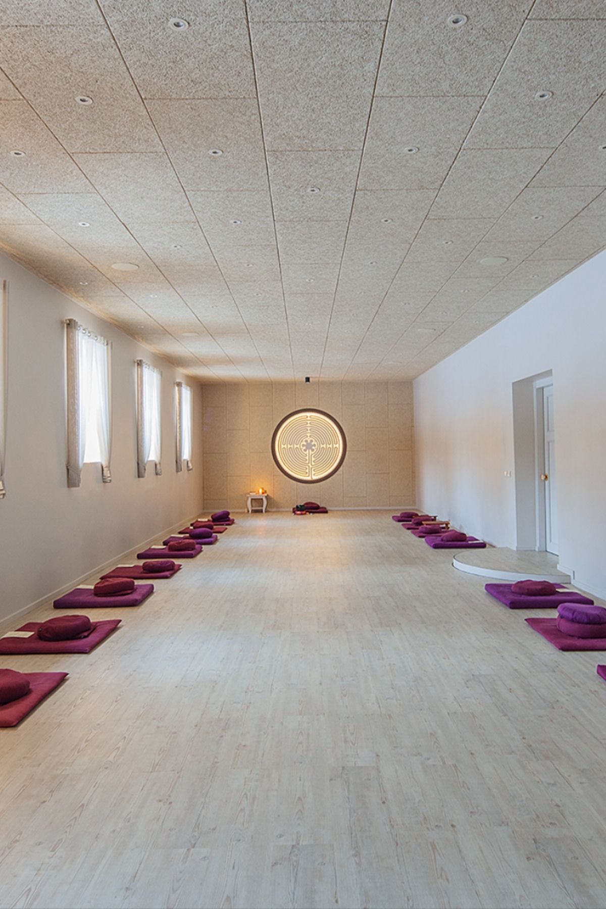 Spacious meditation room featuring a wide drop ceiling with acoustic panels and evenly spaced recessed lights, creating a calm and balanced atmosphere above the wooden floor and neatly arranged floor cushions.